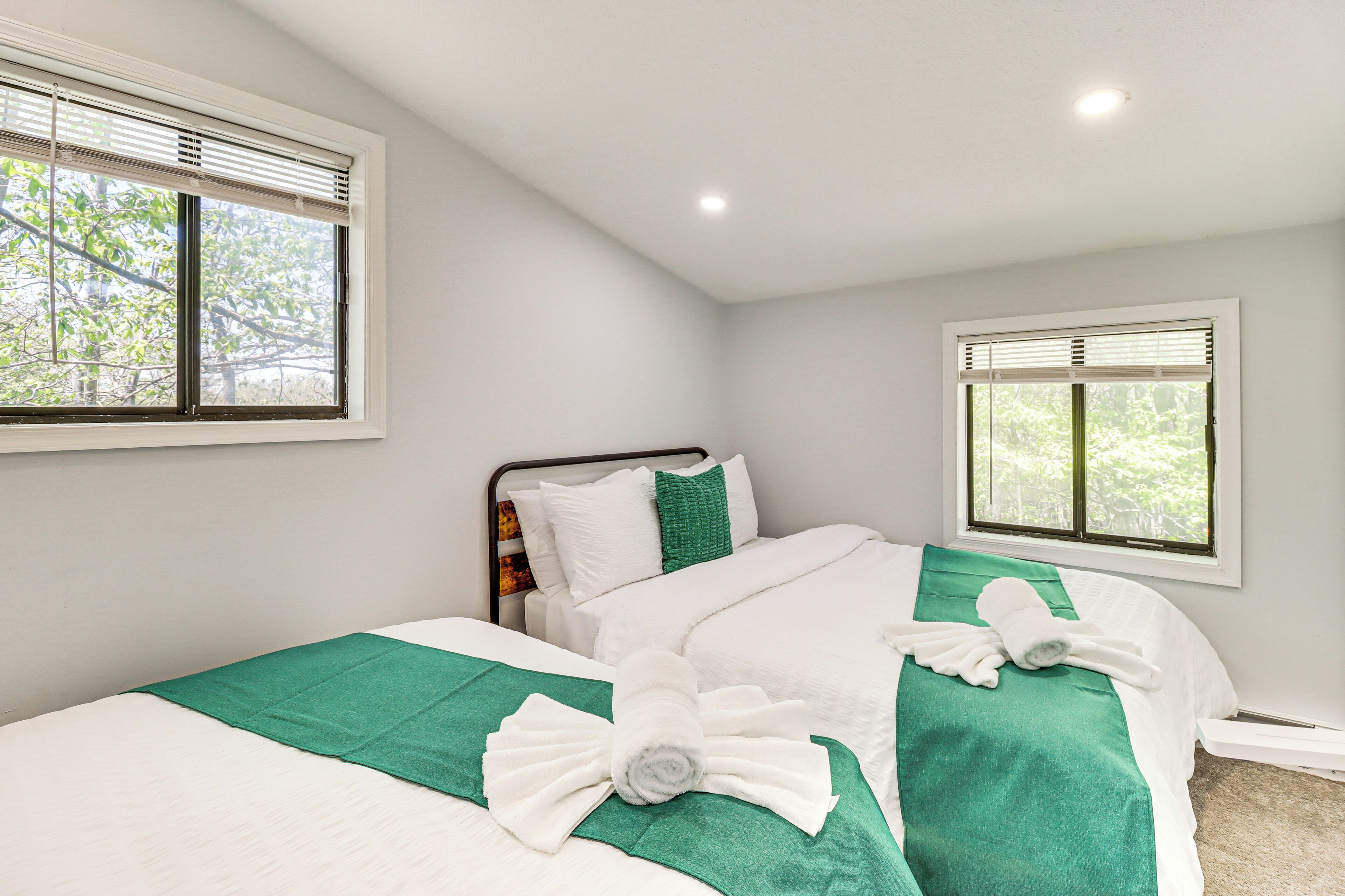 A neatly made bed with white and green bedding, two pillows, and a rolled towel.