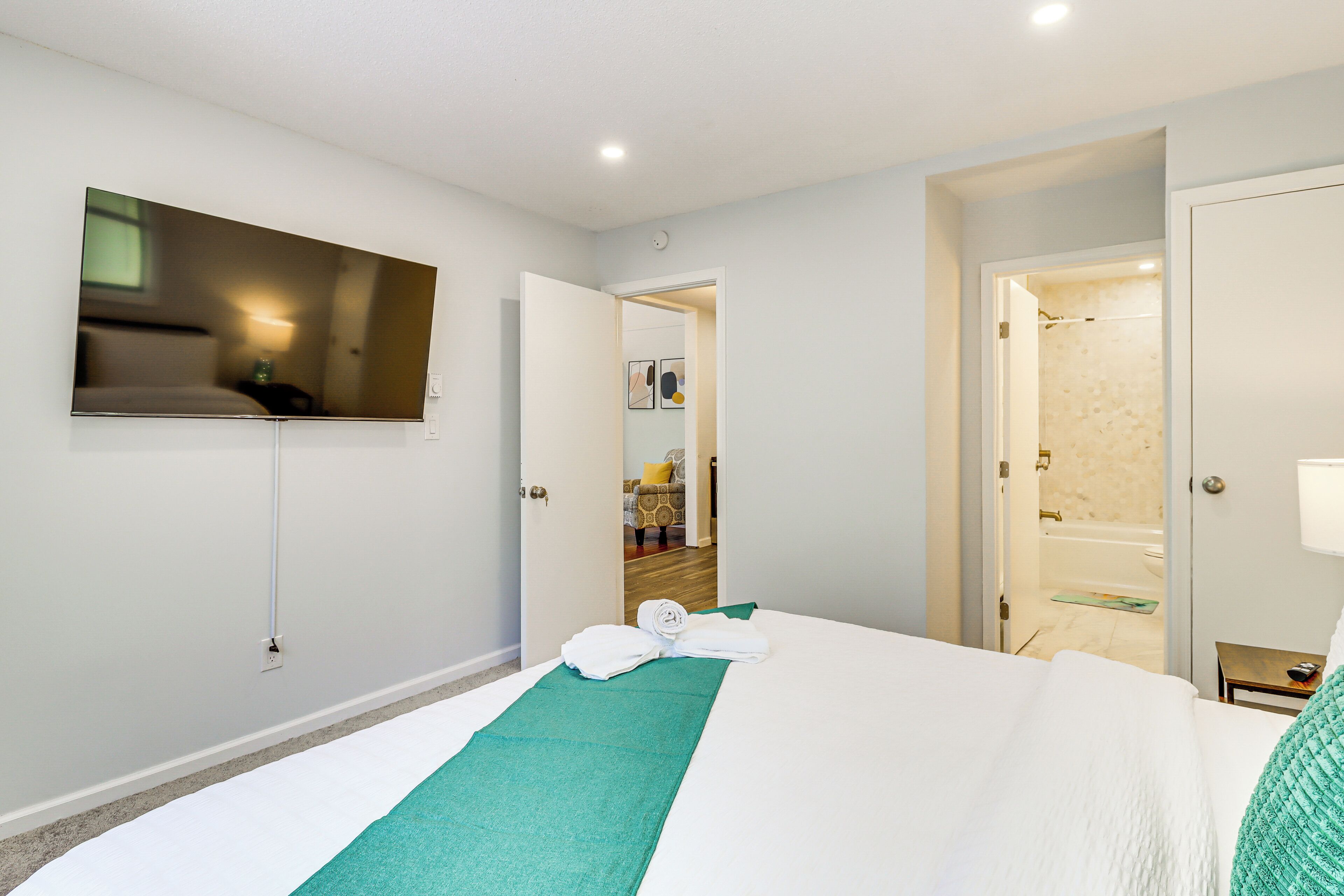 Quarto de hotel com cama, televisão fixada na parede, banheiro com banheira e porta que dá para outro cômodo.