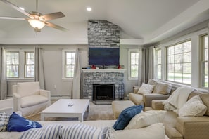 A living room with a stone fireplace, white sofas, a coffee table, and a ceiling fan.