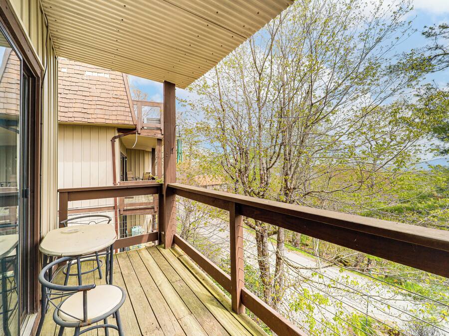 Una terraza de madera con una mesa y sillas, con vistas a una zona residencial con árboles y una casa.