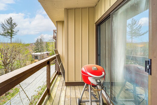 A balcony with a red grill, a wooden railing, and a view of trees and hills. - Walk to Hiking & Skiing: Beech Mountain Condo (Banner Elk)