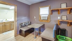 Ein Haustier-freundliches Zimmer mit einer Holzbank, einem kleinen Tisch, einer grünen Transportbox und einem an der Wand befestigten Regal.