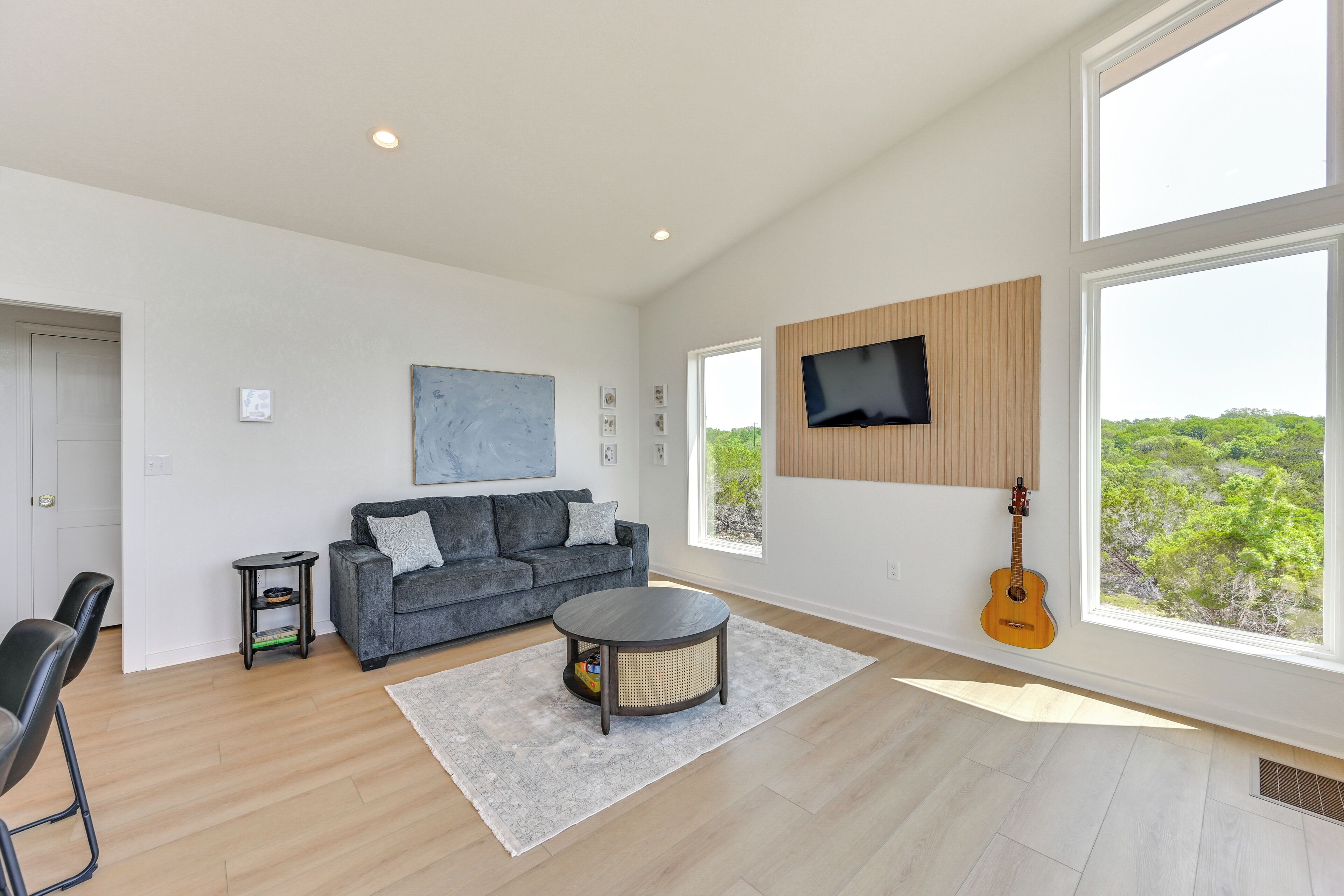 A spacious living room with a grey sofa, a round coffee table, and a guitar leaning against the wall.