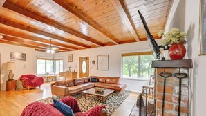 A cozy living room with a wooden ceiling, a leather sofa, a glass coffee table, and a fireplace with a red vase. - Home 3 Mi to Main St Julian: Great for Groups! (Julian)
