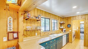 A wooden interior with a kitchen area including a sink, dishwasher, and a window.