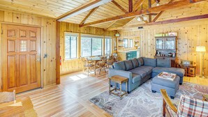 A spacious living room with a large sectional sofa, wooden floors, and a high ceiling with exposed beams.
