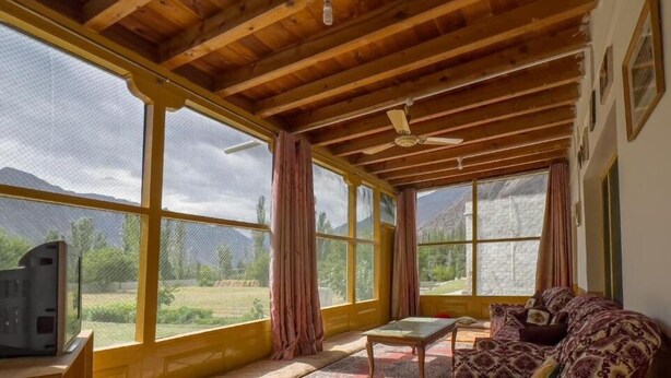 A room with large windows, wooden ceiling beams, a ceiling fan, and a sofa.