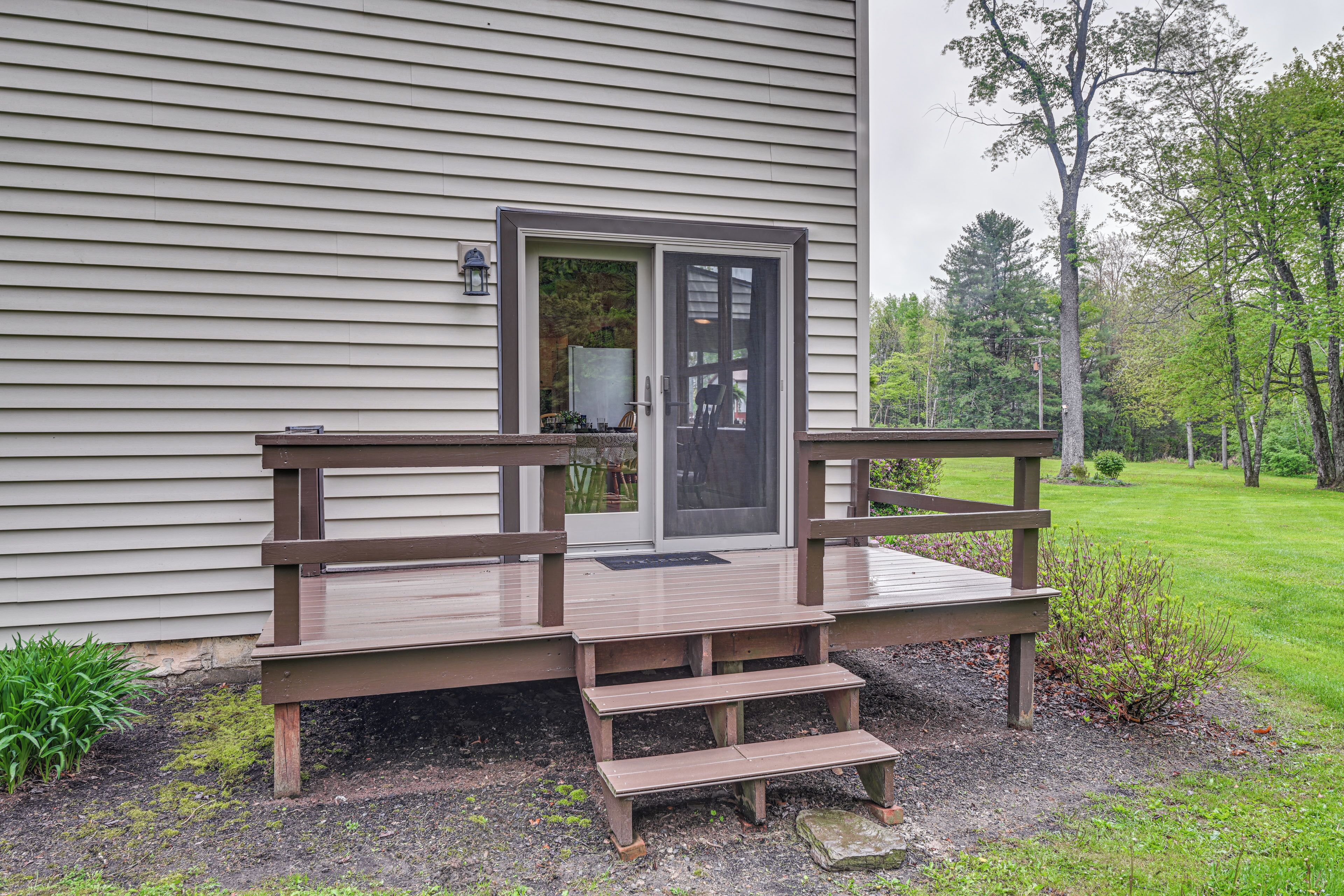 A wooden deck with steps leading to a door, surrounded by a grassy area and trees.