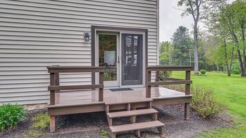 A wooden deck with steps leading to a door, surrounded by a grassy area and trees.