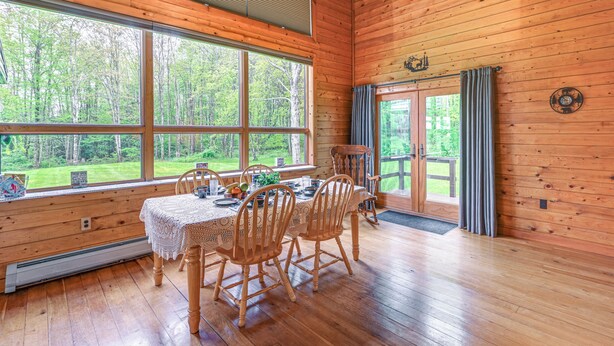 A wooden cabin with a dining area featuring a table set for four, large windows, and a view of the forest. - Near State Parks: Countryside Cottage in Wellsboro (Wellsboro)