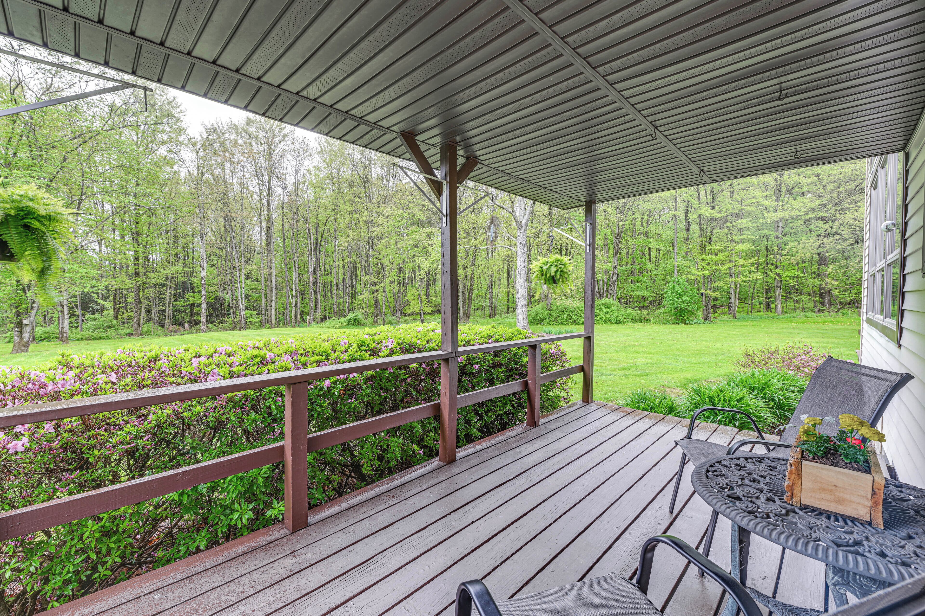 A covered outdoor deck with a wooden railing, a metal table, and chairs.