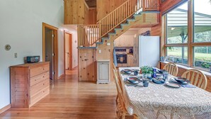 A spacious kitchen with wooden cabinets, a dining area with a lace tablecloth, and a wooden staircase. - Near State Parks: Countryside Cottage in Wellsboro (Wellsboro)