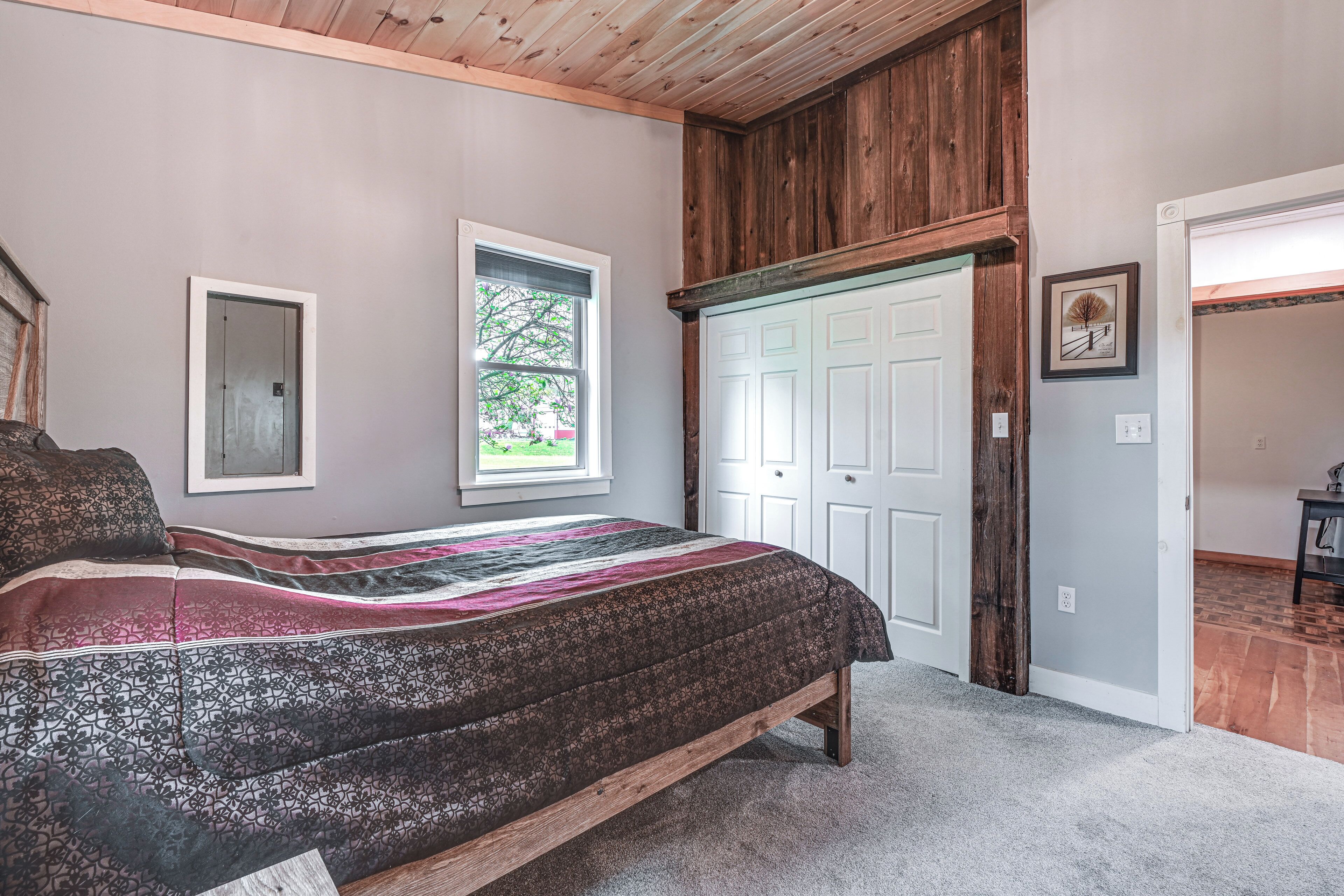 A bedroom with a large bed, a wooden ceiling, a window, and a door.