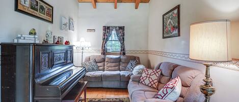 A cozy living room with a piano, a sofa, a lamp, and a rug.