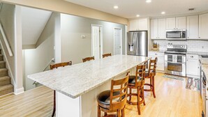 A modern kitchen with a central island, wooden chairs, and stainless steel appliances. - Secluded 6BR Sinclair Lake House w/ Dock (Eatonton)
