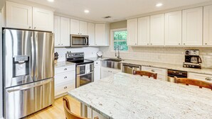 A modern kitchen with white cabinets, stainless steel appliances, and a large marble island. - Secluded 6BR Sinclair Lake House w/ Dock (Eatonton)