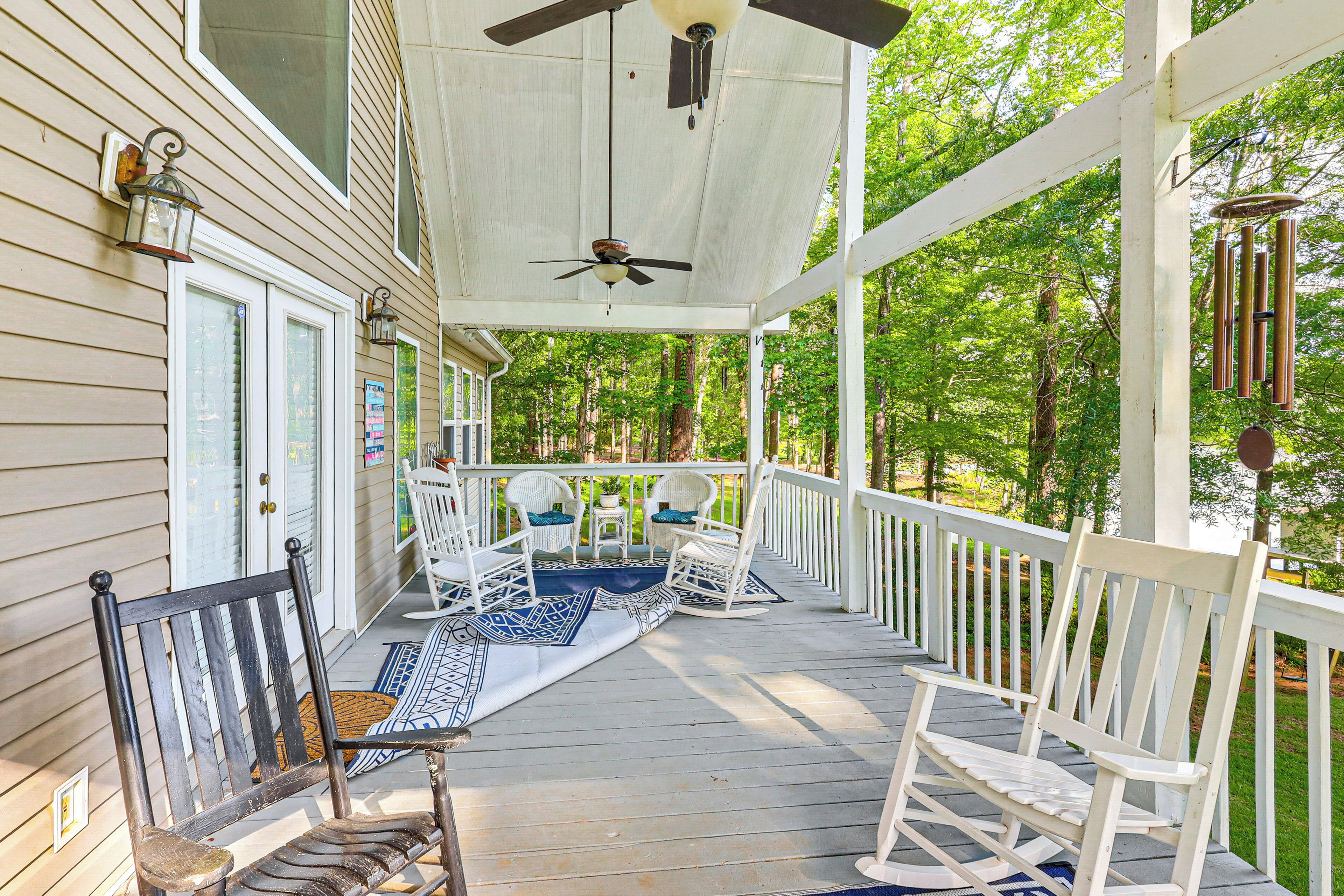 A covered porch with white railings, a ceiling fan, and a view of a forested area.