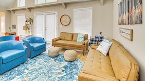 A spacious living room with a large window, a blue armchair, a beige sofa, and a patterned rug. - Secluded 6BR Sinclair Lake House w/ Dock (Eatonton)
