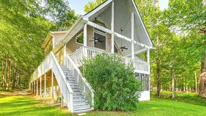 A two-story cabin with a covered porch, a staircase, and a view of the surrounding forest. - Secluded 6BR Sinclair Lake House w/ Dock (Eatonton)