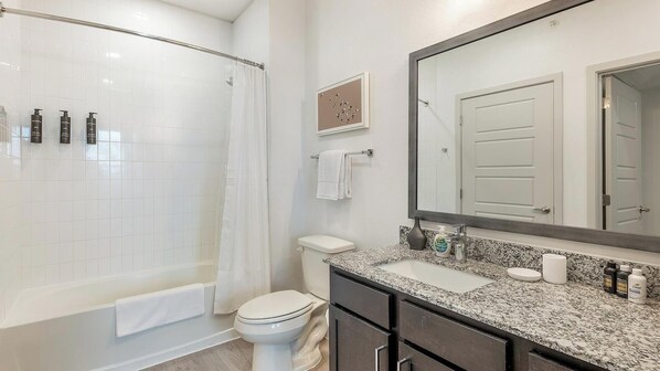 A bathroom with a shower, toilet, sink, and a large mirror.