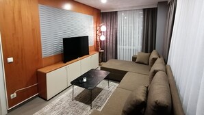 A modern living room with a flat-screen TV on a wooden console, a black coffee table, a beige sofa, and a patterned rug. - Non-Smoked Apartments at Levent (İstanbul)