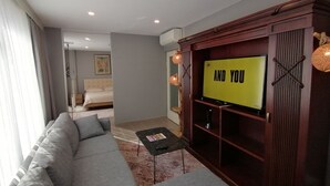 A modern living room with a large flat-screen TV mounted on a wooden cabinet, a grey sofa, and a small coffee table. - Non-Smoked Apartments at Levent (İstanbul)
