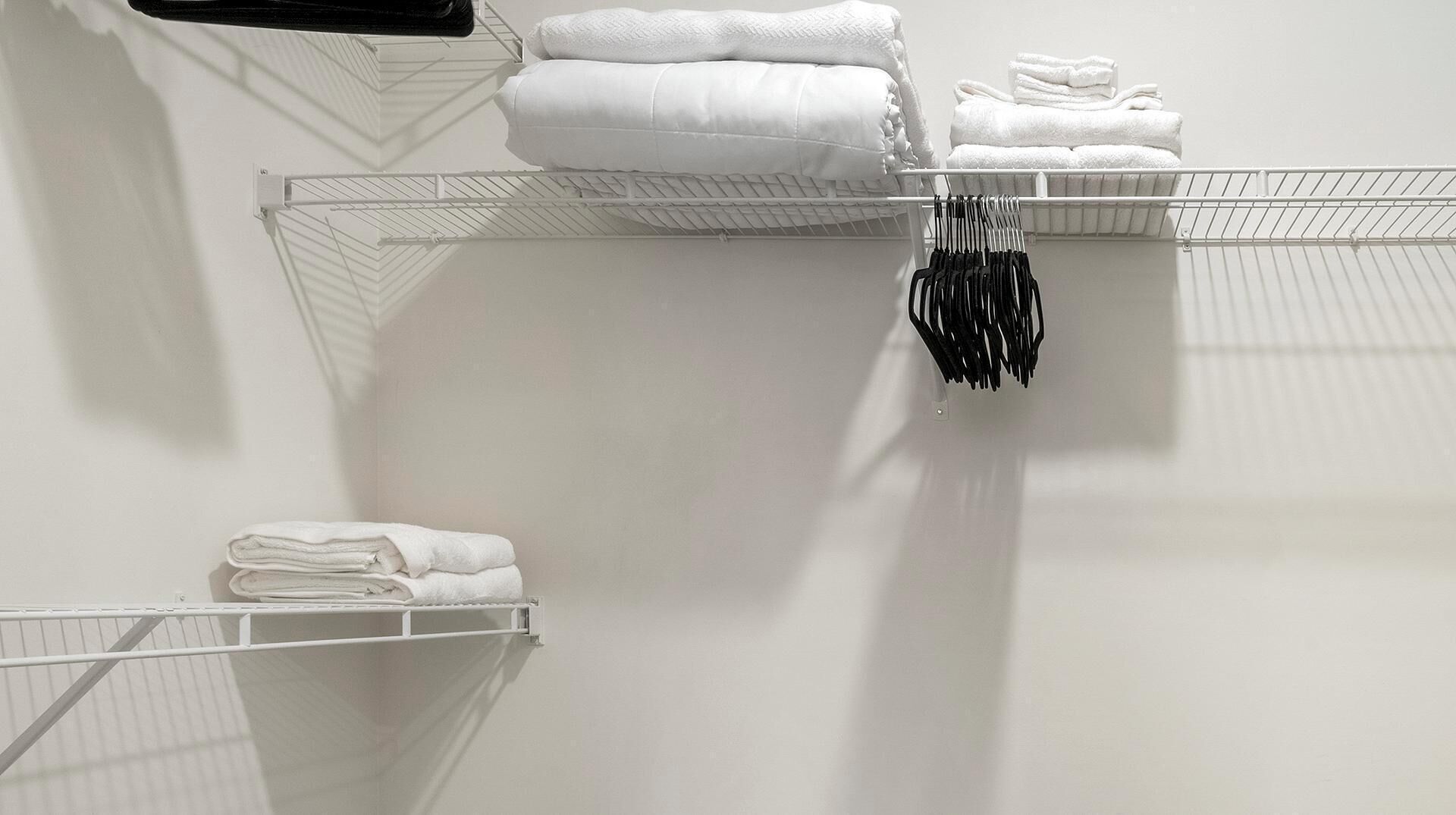 A storage area with white shelves holding folded towels and a rack with black hangers.