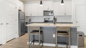 A kitchen with white cabinets, a granite countertop, a stainless steel refrigerator, a microwave, and a stove.