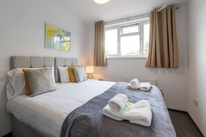 Una habitación de hotel con una cama grande, una mesita de noche, una ventana con cortinas y un cuadro en la pared.