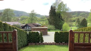 Blick auf ein hölzernes Tor, das zu einem Gebäude mit einem Ziegeldach führt, umgeben von gepflegten Hecken und einer Rasenfläche.