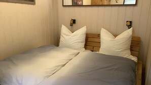 Ein Bett mit weißer Bettwäsche und einem Holz-Kopfteil, ein Nachttisch mit Lampe sowie ein an der Wand befestigter Bilderrahmen.