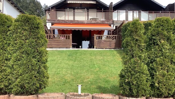 Ein zweistöckiges Holzhaus mit Balkon, überdachter Terrasse und gepflegtem Rasen.