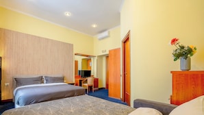 Quarto de hotel com duas camas, uma escrivaninha, uma cadeira e um guarda-roupa de madeira.