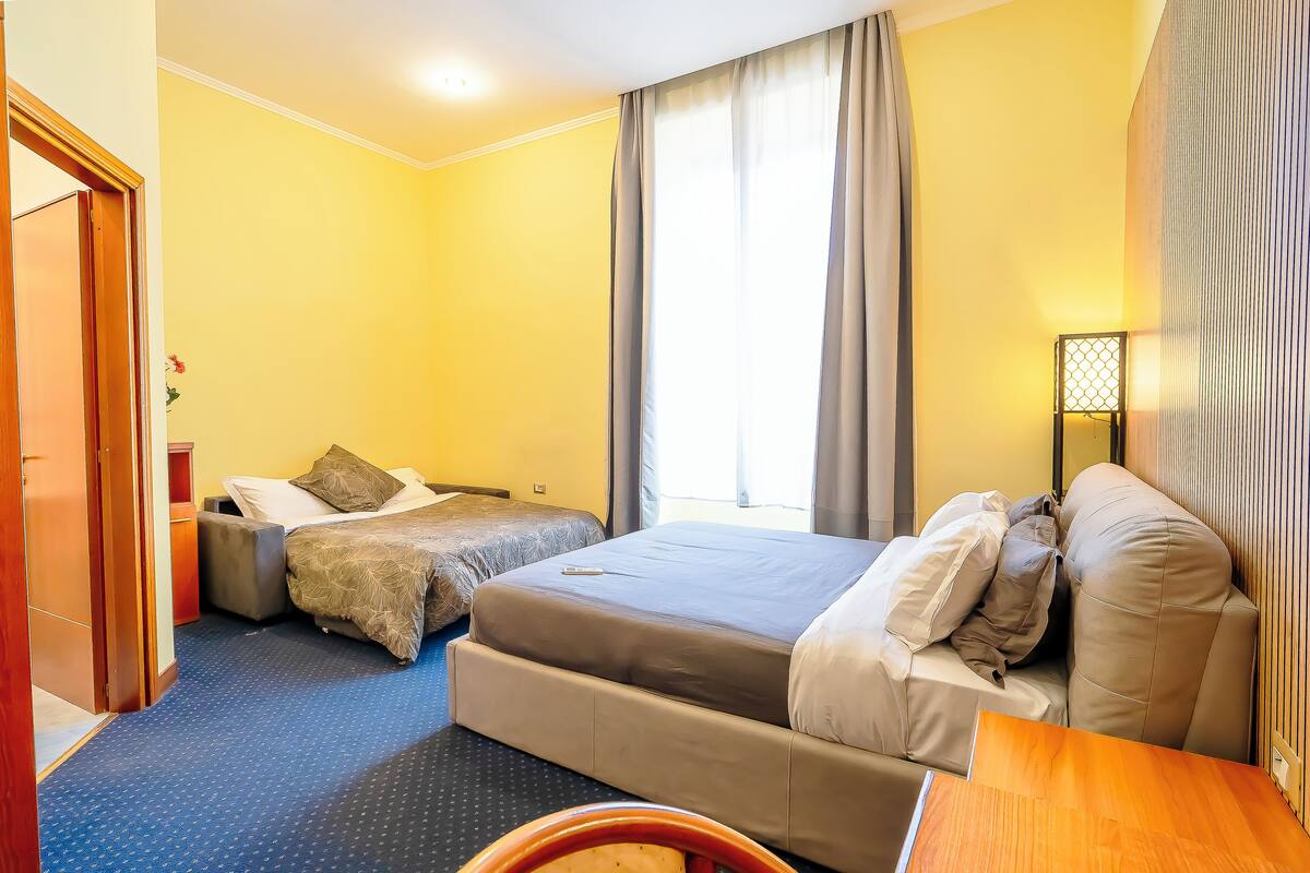 A hotel room with a large bed, a smaller bed, a desk, and a wardrobe.