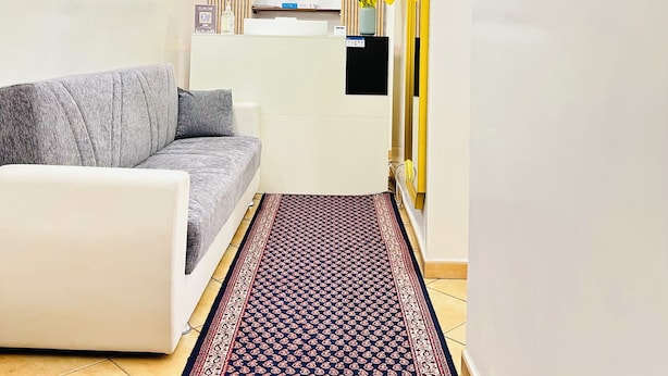 Uma sala de estar moderna com um sofá cinzento, um tapete estampado, uma prateleira na parede e um espelho.