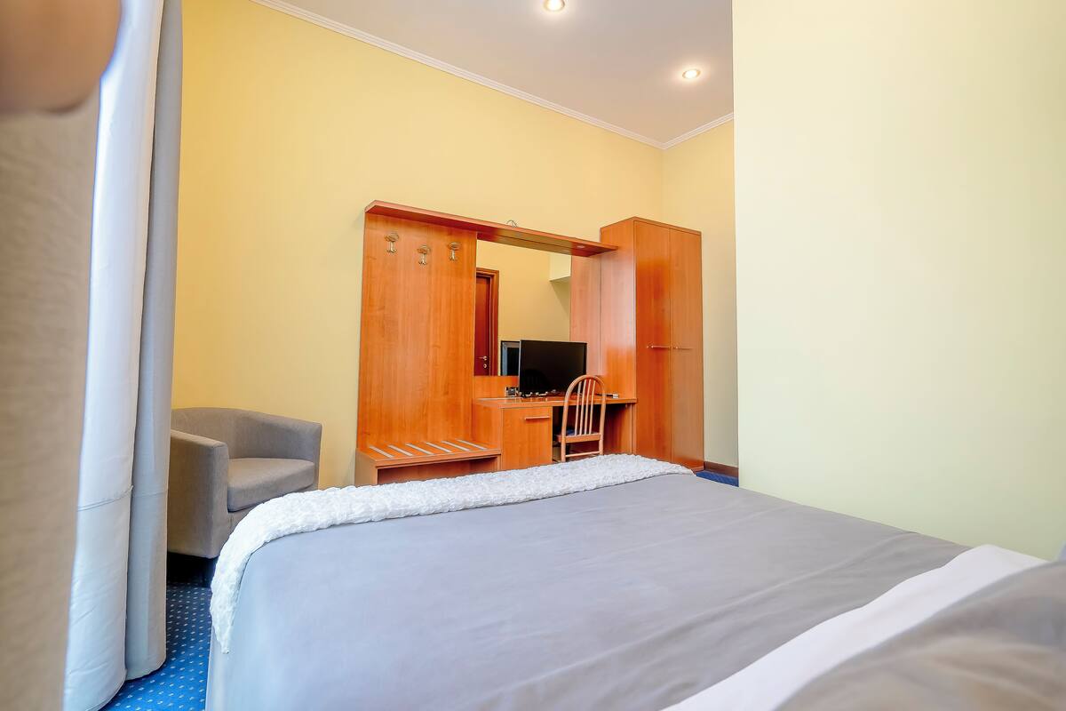 A hotel room with a bed, a desk with a chair, a television, and a wardrobe.