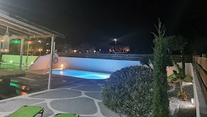 Een nachtzicht van een zwembad met een overdekte zithoek en een stadszicht op de achtergrond.