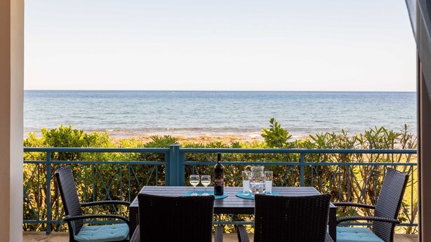 A table with chairs and a bottle of wine, overlooking a beach. - Agrilos Seafront Serenity - Waterfront Oasis (Trifylia)