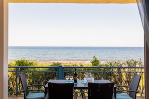 A table with chairs and a bottle of wine, overlooking a beach. - Agrilos Seafront Serenity - Waterfront Oasis (Trifylia)
