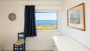 A room with a view of the sea, a chair, a table, a framed picture, and a decorative plate on the wall. - Agrilos Seafront Serenity - Waterfront Oasis (Trifylia)
