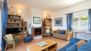A living room with a fireplace, sofas, a television, and bookshelves. - Agrilos Seafront Serenity - Waterfront Oasis (Trifylia)