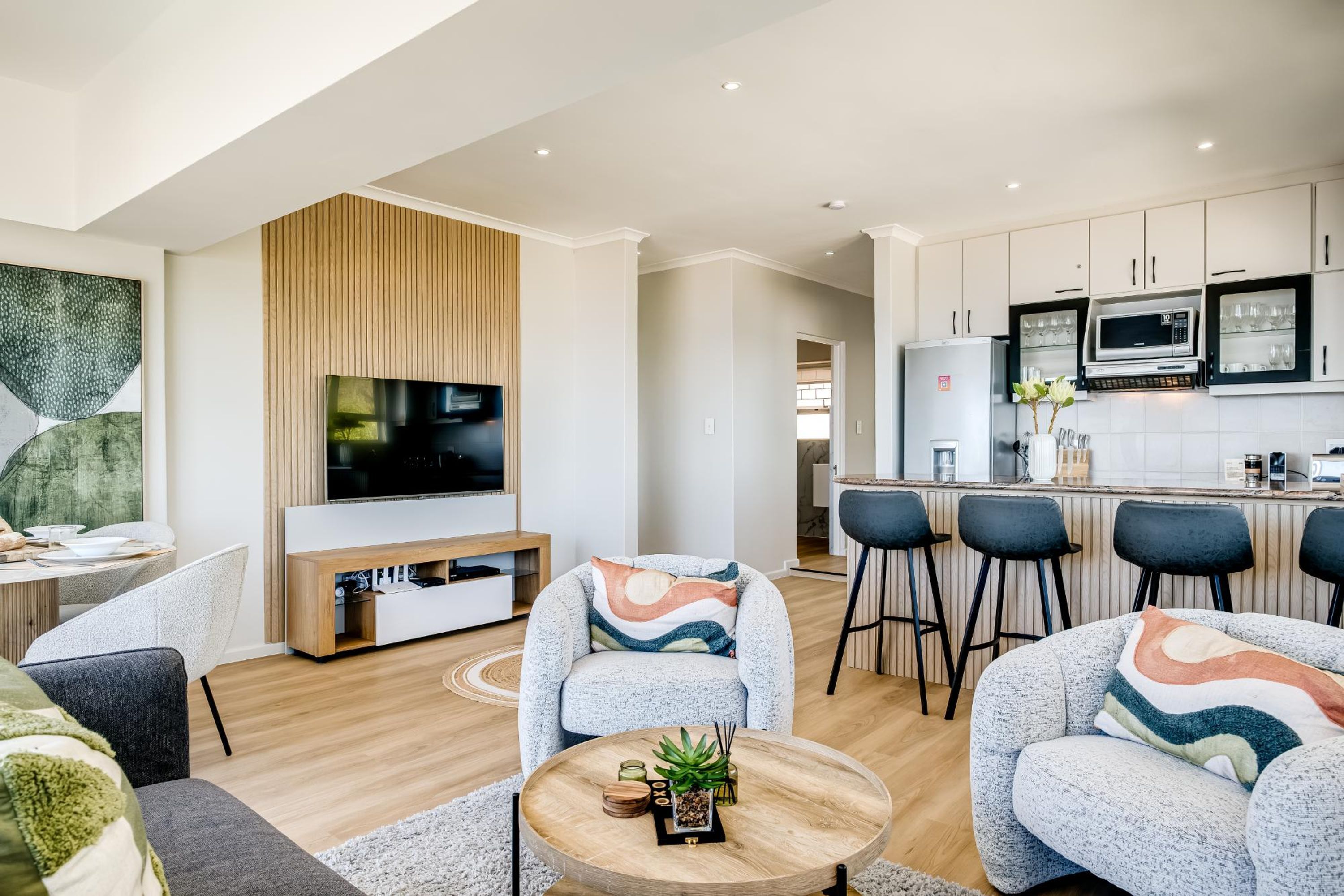 Una sala de estar moderna con televisor, sofás, una mesa de centro y una zona de cocina con taburetes de bar.