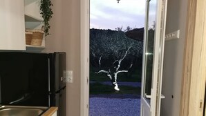 Eine schmale Küche mit Spüle, einem schwarzen Kühlschrank und einer Tür zu einem Garten mit einem Baum.