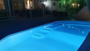 Ein Pool mit Stufen, umgeben von einer überdachten Terrasse mit Lichterketten.