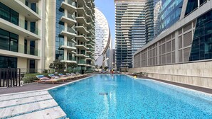 A swimming pool with lounge chairs, surrounded by modern high-rise buildings. - The Art of Living Missoni Inspired Luxury Studio (Dubai)