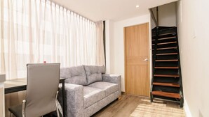 A modern living room with a grey sofa, a dining table with chairs, a wooden door, and a staircase. - NOK Amazing Duplex in Parque 93 (Bogotá)