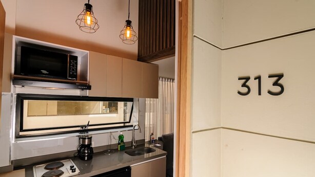 A compact kitchen with a microwave, stove, and sink. The number 313 is displayed on the wall. - NOK Amazing Duplex in Parque 93 (Bogotá)