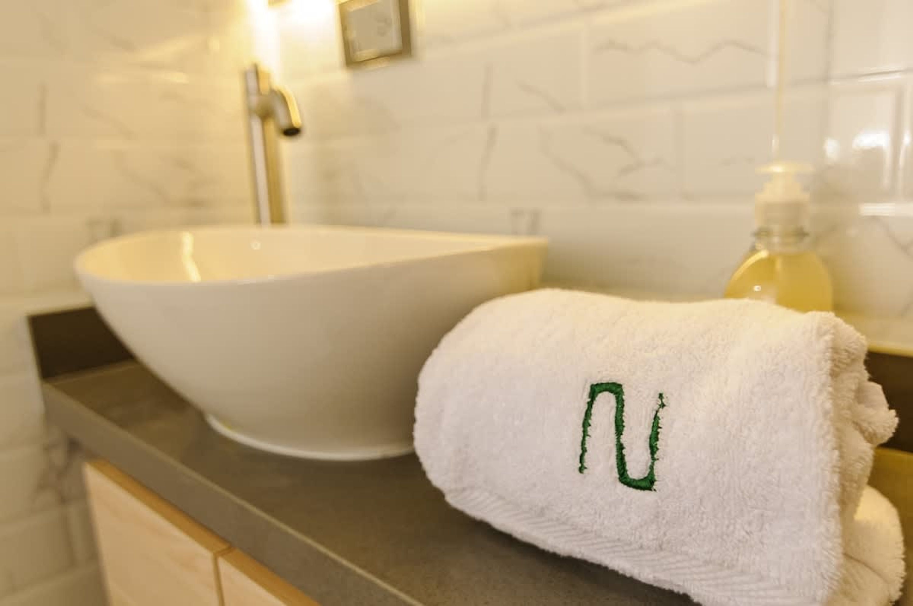 Ein Badezimmer mit einem weißen Waschbecken, einem Handtuch mit grünem 'N' und einer Seifenflasche.