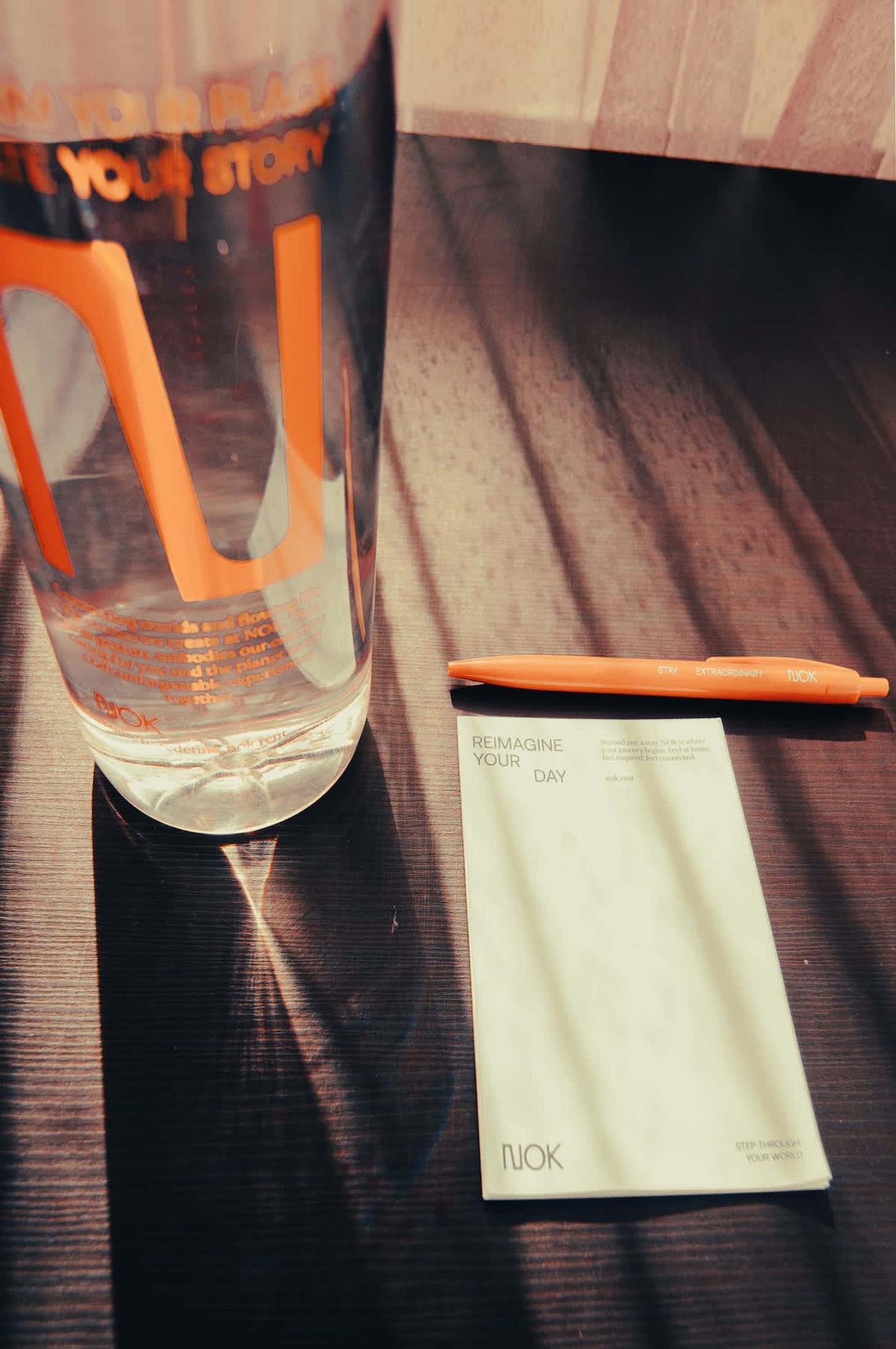 Ein Glas mit Trinkhalm, ein Stift und eine Karte auf einer Holztischplatte.
