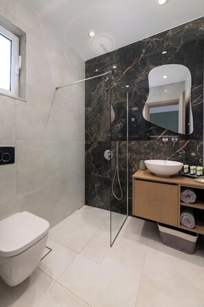 A modern bathroom with a glass-enclosed shower, a white toilet, a marble backsplash, and a wooden vanity with a large sink.